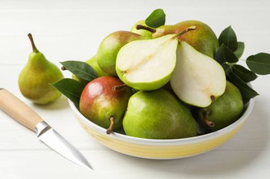 Taze armutlar, bıçak ve yeşil yapraklar beyaz ahşap masada, yakın plan.