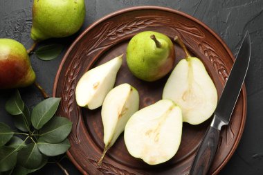 Taze armutlar, bıçak ve yeşil yapraklar siyah masada, düz yerde.