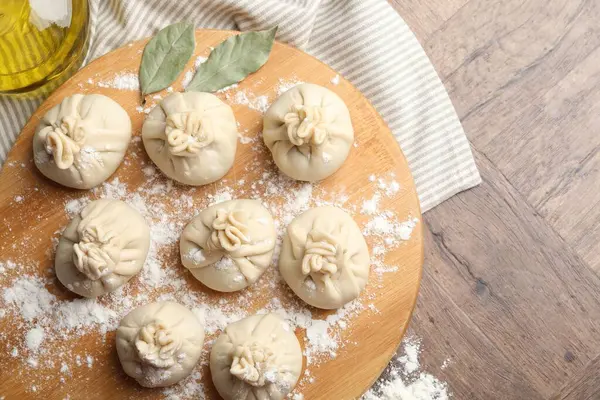 Ahşap masa üzerinde un, yağ ve defne yapraklarıyla pişirilmemiş khinkaliler (hamur tatlısı). Metin için boşluk