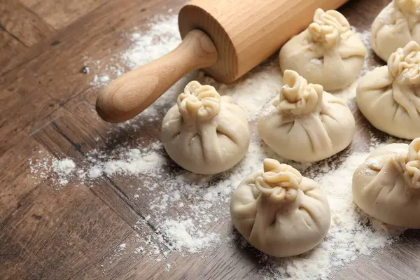 Ahşap masa üzerinde merdane ve un ile pişirilmemiş khinkaliler (hamur tatlısı), yakın plan