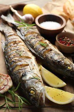 Ahşap masada biberiye ve limonla servis edilen lezzetli kavrulmuş deniz kabuğu balığı, yakından. Ev yapımı deniz ürünleri yemeği.