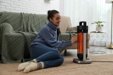 Evdeki elektrikli ısıtıcının yanında elini ısıtan kadın.