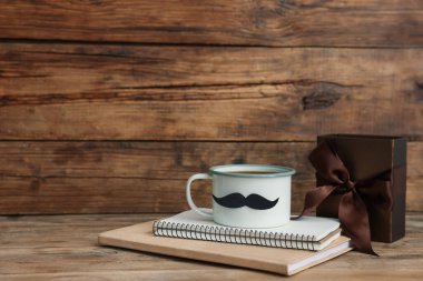 Babalar Günün kutlu olsun. Bıyıklı fincan, defterler ve tahta masada hediye. Metin için boşluk