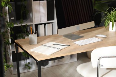 Modern bilgisayarı, kırtasiyesi ve çiçek dekoru olan şık bir iş yeri. Biyofilik iç tasarım