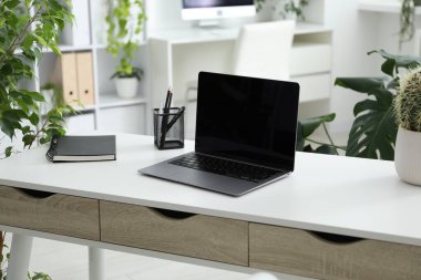 Ofisinde dizüstü bilgisayarı, kırtasiyesi ve çiçek dekoru olan şık bir iş yeri. Biyofilik iç tasarım