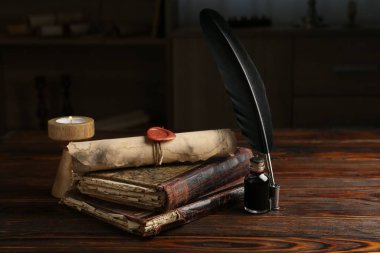 Yuvarlanmış parşömen, yanan mum, tüy, mürekkep hokkası ve ahşap masadaki kitaplar.