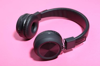 Pembe arka planda bir çift şık siyah kulaklık, yakın plan.