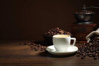 Kahverengi arka plan, kahve fincanı, fasulye ve öğütücü ahşap masa, metin için yer