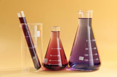 Bej arka planda renkli sıvılar bulunan laboratuvar camları.