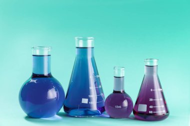 Turkuaz arka planda renkli sıvılar bulunan laboratuvar camları.