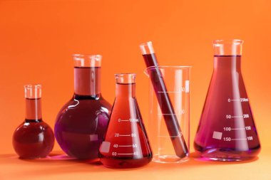 Turuncu zemin üzerinde kırmızı sıvı bulunan laboratuvar camları.