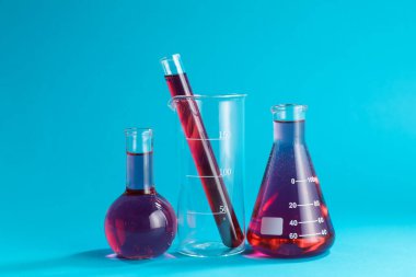 Açık mavi zemin üzerinde renk sıvısı bulunan laboratuvar camları