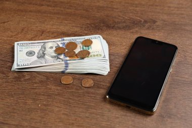 Akıllı telefon, dolar ve paralar ahşap masada, yakın plan.