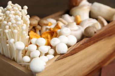 Masadaki ahşap sandıkta farklı çiğ mantarlar, yakın plan.