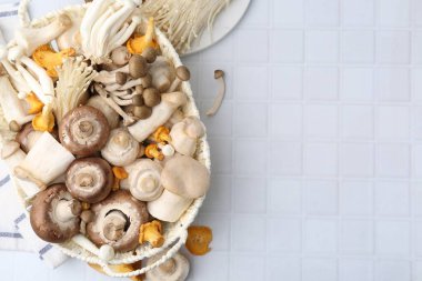 Hasır sepetteki farklı çiğ mantarlar beyaz fayanslı masada, düz yerde. Metin için boşluk