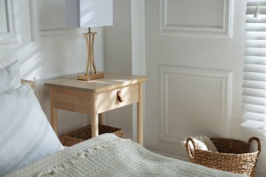 Yatağın yanında lamba olan komodin.