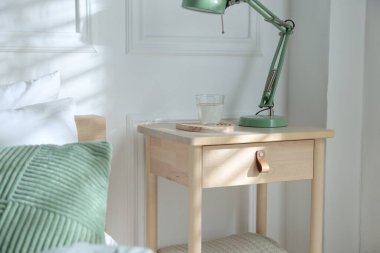 Yatak odasının yanında lamba ve bir bardak su olan komodinin yanında.