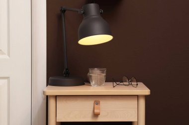 Bir bardak su, lamba ve gözlüklü ahşap masa.