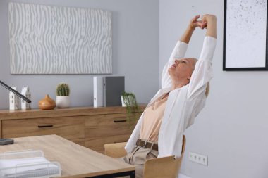 Gri duvarın yanındaki masada uzanan olgun bir kadın.