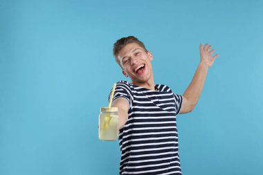 Açık mavi arka planda limonata kavanozu olan mutlu bir adam. Tazeleyici içecek.