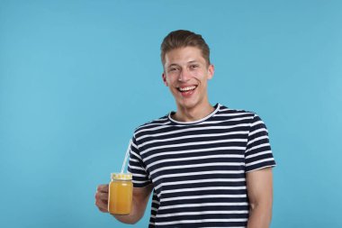 Açık mavi arka planda portakal suyu kavanozu olan mutlu bir adam. Tazeleyici içecek.
