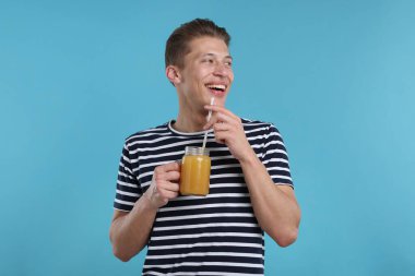 Açık mavi arka planda portakal suyu kavanozu olan mutlu bir adam. Tazeleyici içecek.