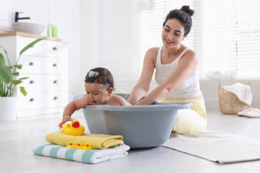 Anne küçük bebeğini evde yıkıyor.