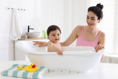 Anne küçük bebeğini evde yıkıyor.