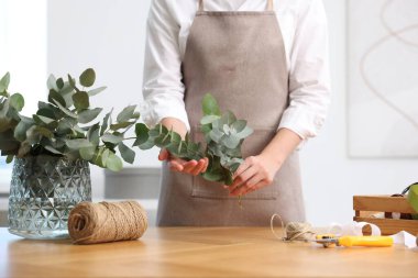 Çiçekçinin ahşap masasında okaliptüs dallarından güzel bir buket yapıyor.