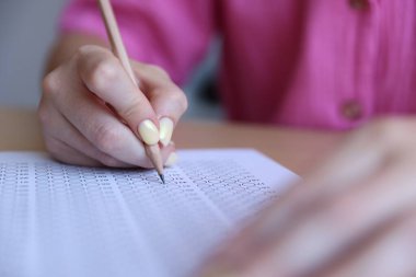 Öğrenci masadaki çoklu seçim testini dolduruyor, yakın çekim. Sınavı geçmek