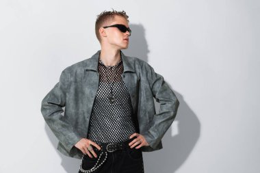 Beyaz arka planda şık ceket ve güneş gözlüğü takan yakışıklı bir genç.