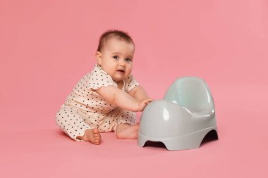 Küçük şirin bebek pembe arka planda lazımlığın yanında oturuyor.