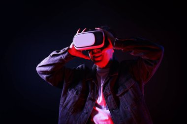 Gülümseyen adam sanal gerçeklik kulaklığını kullanarak neon ışıklarda siyah arka plana karşı
