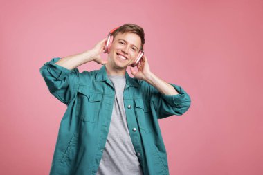Kulaklıkla müzik dinleyen ve pembe arka planda dans eden mutlu bir adam.