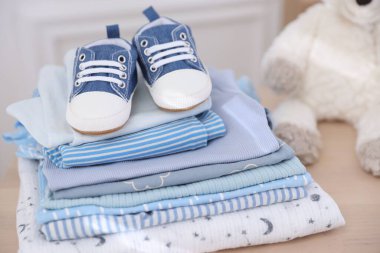 İçerideki ahşap masada temiz bebek kıyafetleri ve ayakkabılar yığını.