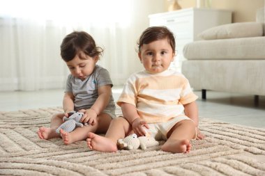 Evde yerde oyuncaklarla oynayan şirin ikiz bebekler.