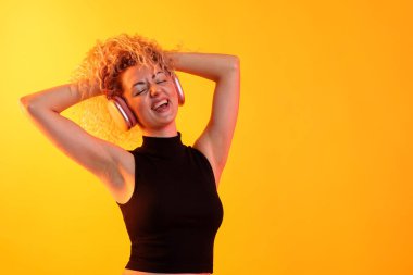 Kulaklıkla müzik dinleyen ve sarı arka planda dans eden mutlu kadın. Metin için boşluk