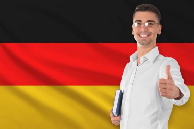 Almanya bayrağına başparmak işareti gösteren kitabı olan bir öğretmen. Dil okulu