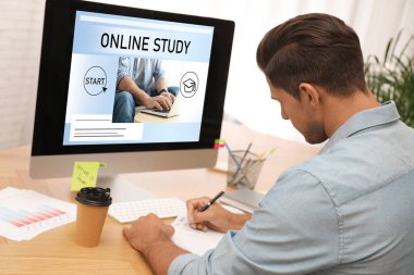 Çevrimiçi çalışma. Masada e-öğrenim için bilgisayar kullanan bir adam