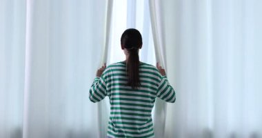 Kadın evde pencere perdelerini açıyor, arka manzara