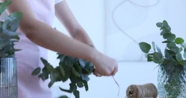 Çiçekçinin ahşap masasında okaliptüs dallarından güzel bir buket yapıyor.