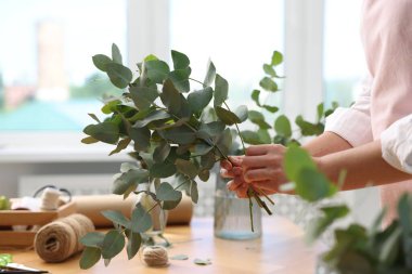 Çiçekçinin ahşap masasında okaliptüs dallarından güzel bir buket yapıyor.