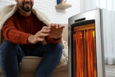 Evdeki elektrikli ısıtıcının yanında ellerini ısıtan adam, yakın çekim.