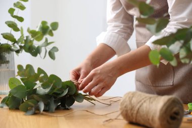 Çiçekçinin ahşap masasında okaliptüs dallarından güzel bir buket yapıyor.