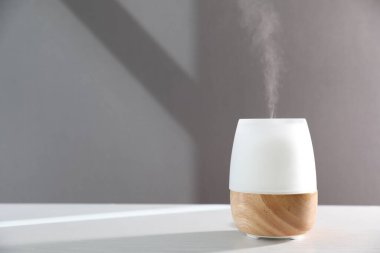 Beyaz ahşap masada gri arka planda modern aroma lambası. Metin için boşluk