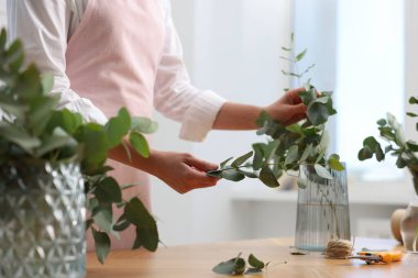 Çiçekçinin ahşap masasında okaliptüs dallarından güzel bir buket yapıyor.