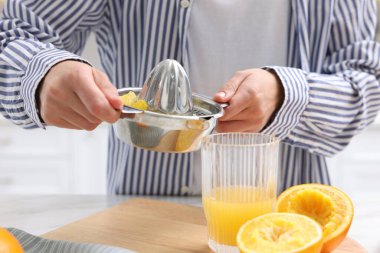 İçerideki masada taze sıkılmış portakal suyunu bardağa dolduran kadın, yakın plan.