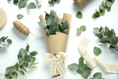 Çiçekçi. Beyaz masa üzerinde okaliptüs dalları, iplikler, kurdele ve ambalaj kağıdı düz.