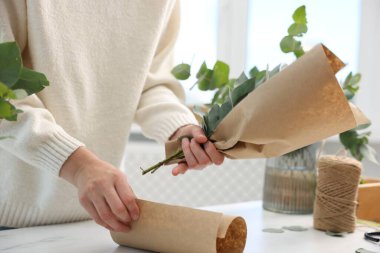 Çiçekçinin beyaz mermer masasında okaliptüs dallarından güzel bir buket yapıyor.