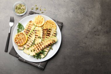 Gri desenli masada servis edilen balkabağı tohumlu, limonlu ve maydanozlu lezzetli ızgara kabak dilimleri. Metin için boşluk